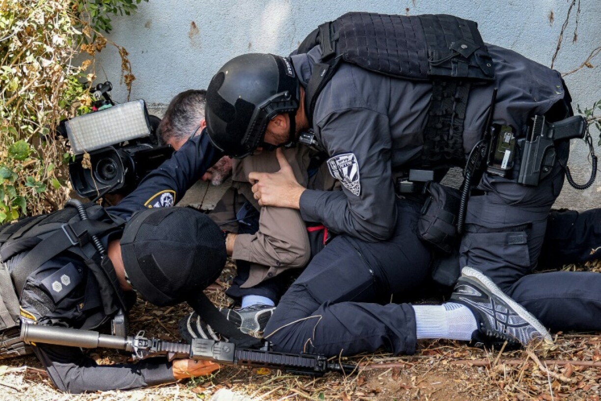 Des policiers israéliens et un journaliste se mettent à l'abri pendant une alerte à la roquette à Sdérot, en Israël, le 12 octobre 2023