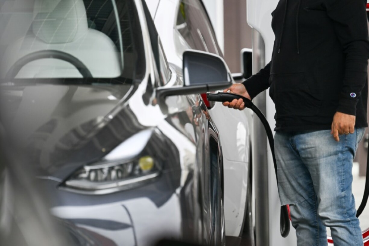 A driver plugs in a Tesla electric vehicle to charge at a Tesla Supercharger location in Santa Monica, California