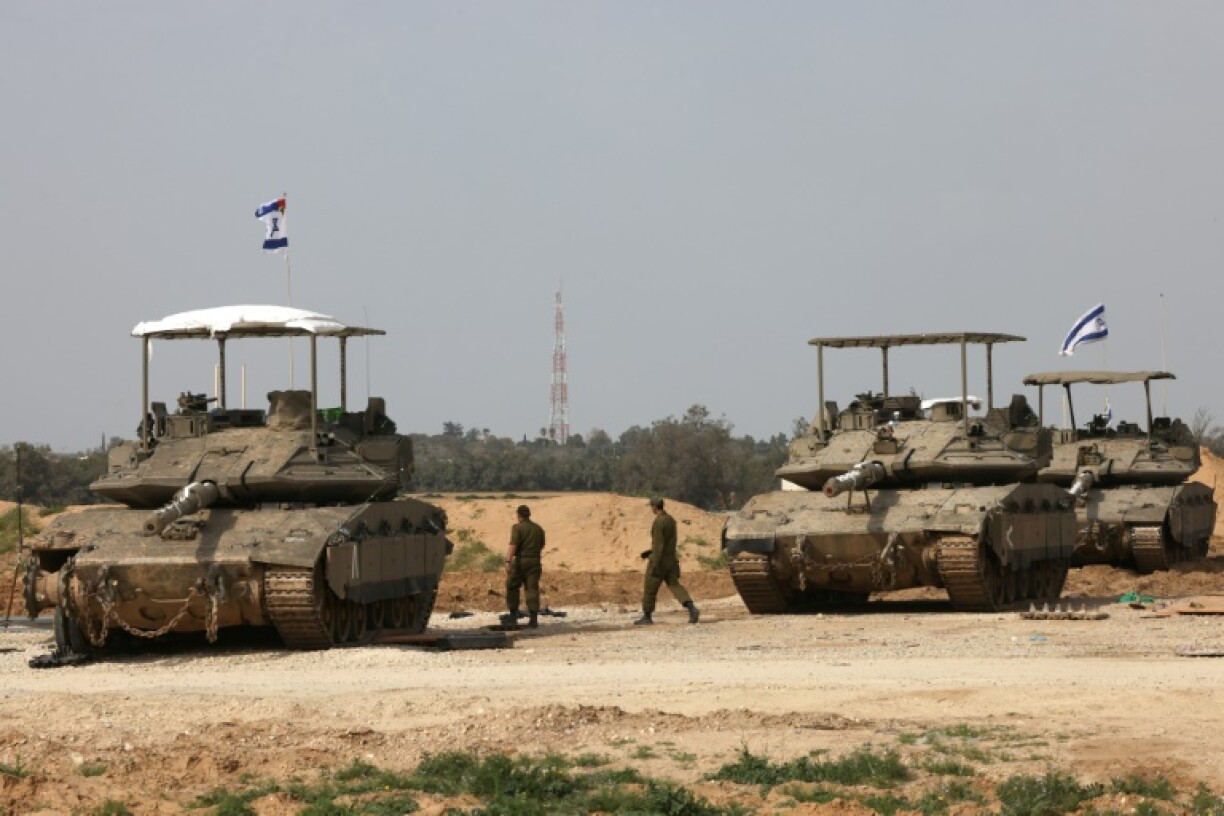 Israeli army soldiers walk past tanks at a position near Israel's southern border with the Gaza Strip