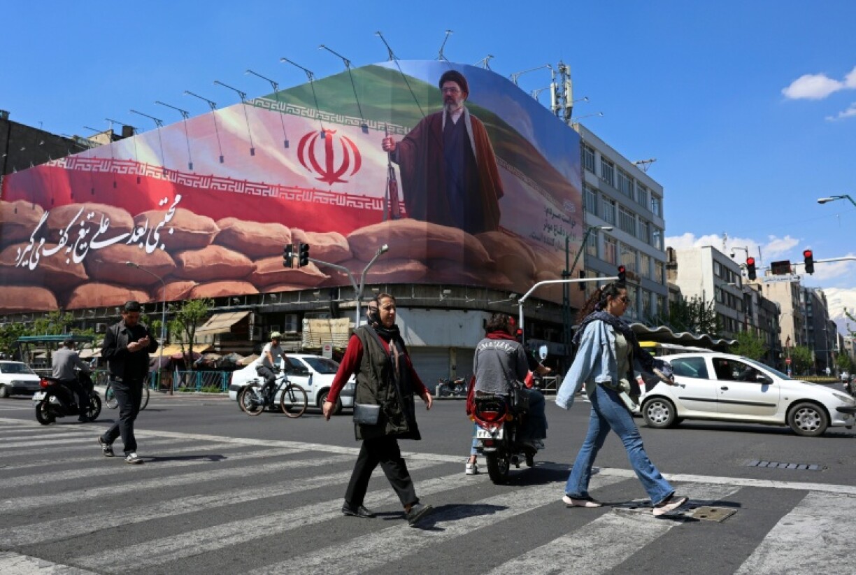 Des piétons traversent une rue devant une affiche géante du guide suprême iranien, l'ayatollah Mojtaba Khamenei, le 10 avril 202 à Téhéran