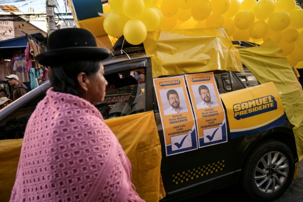 A Bolivian Indigenous woman walks past a car with campaign posters of Bolivian presidential candidate Samuel Doria Medina