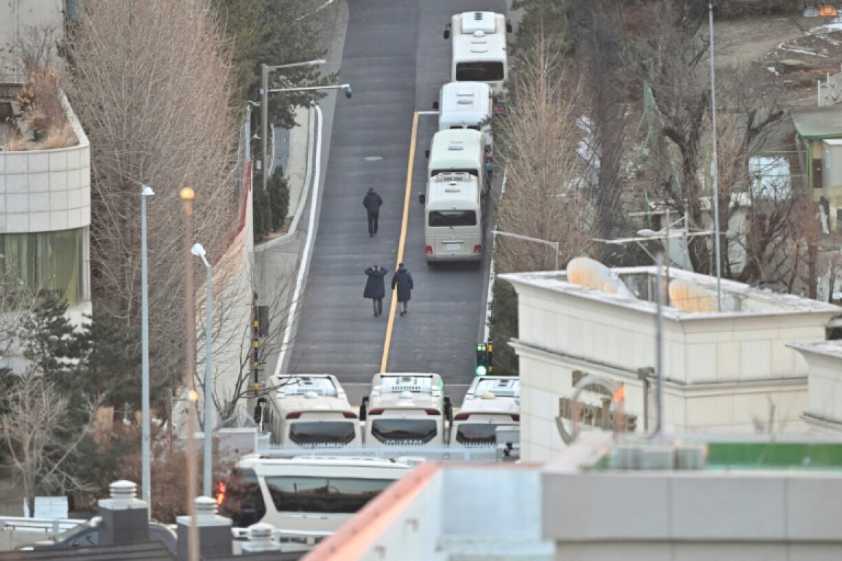 Security personnel walk on a road lined up with buses blocking the entrance gate to protect impeached South Korean president Yoon Suk Yeol