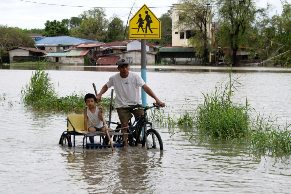 A father and child ride a tricycle through a flooded street in a village north of Manila on Friday
