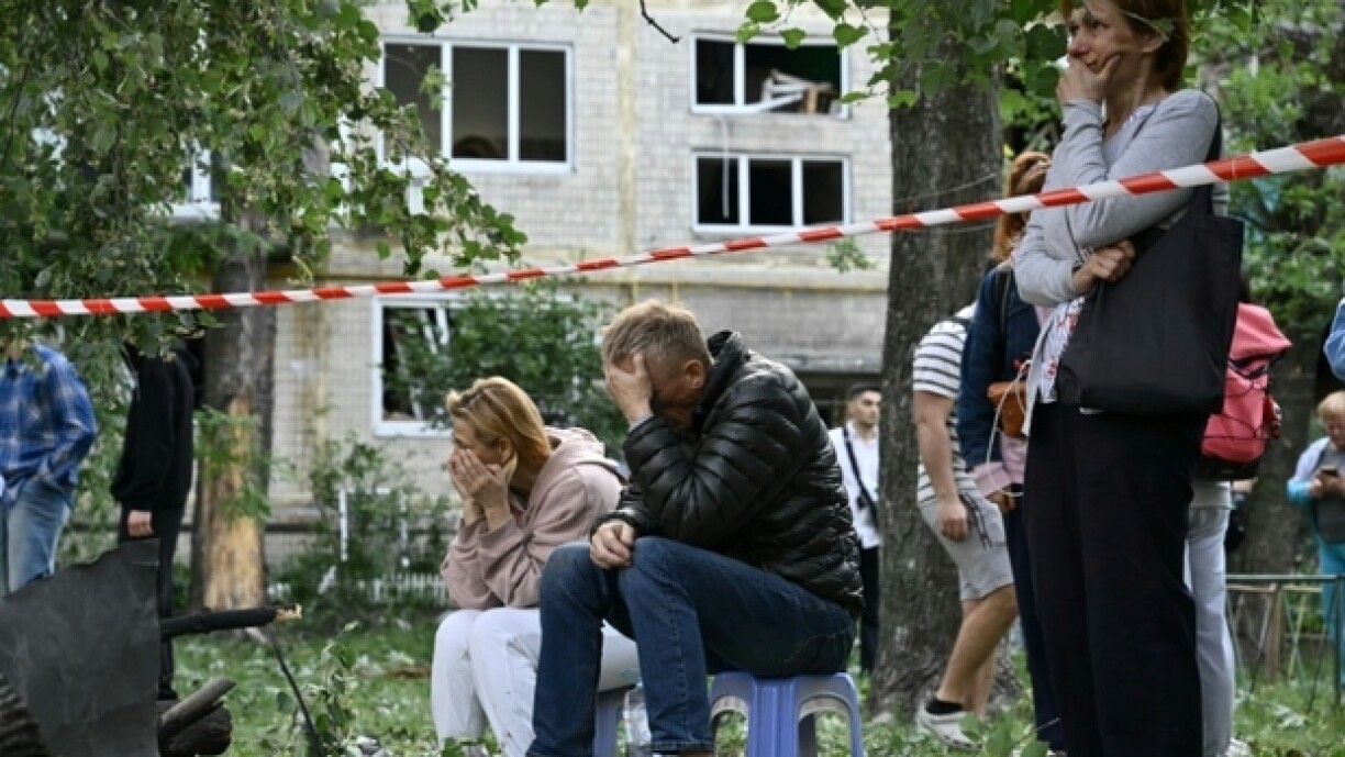 Des habitants en état de choc attendent pendant que des sauveteurs ukrainiens effectuent des recherche dans un immeuble résidentiel fortement endommagé par une frappe de missile russe, le 17 juin 2025 à Kiev